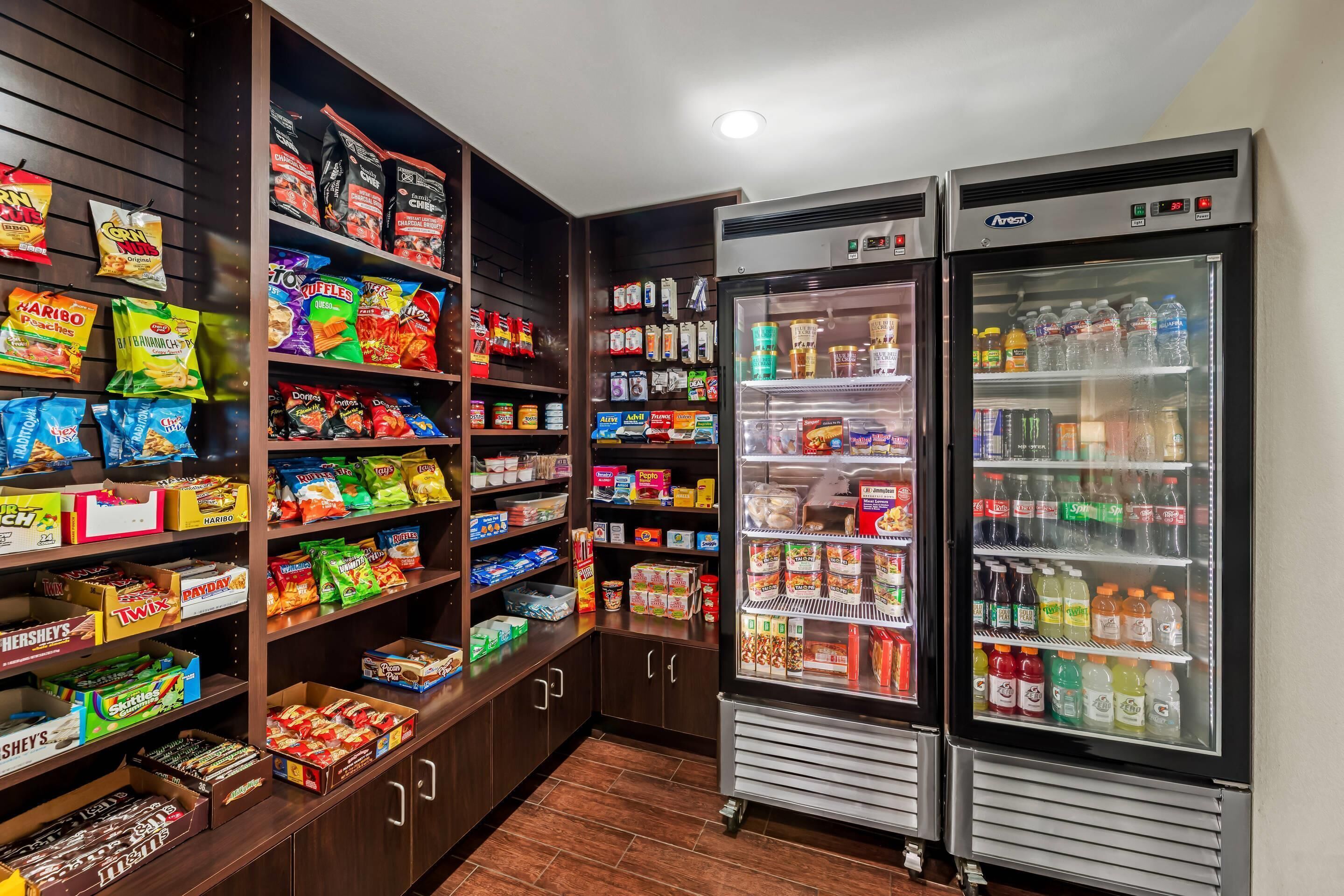Una sección de aperitivos y bebidas con estantes llenos de diferentes productos y dos dispensadores de líquidos.