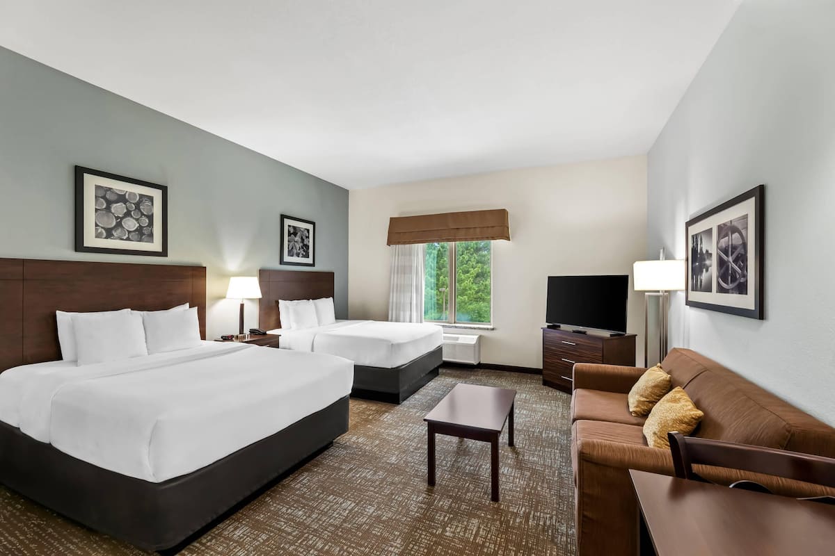 A hotel room with two beds, a sofa, a TV, and framed pictures on the walls.