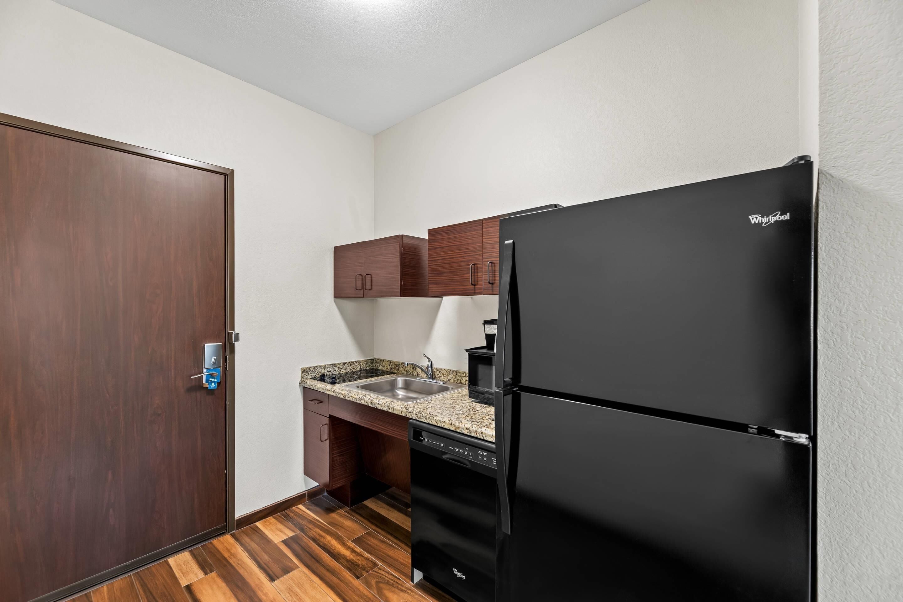 A compact kitchen with a black Whirlpool refrigerator, wooden cabinets, a granite countertop, and a dishwasher.