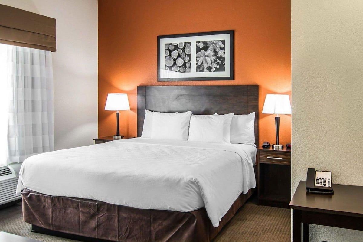 A hotel room with a large bed, two bedside lamps, a framed picture on the wall, and a desk with a phone.