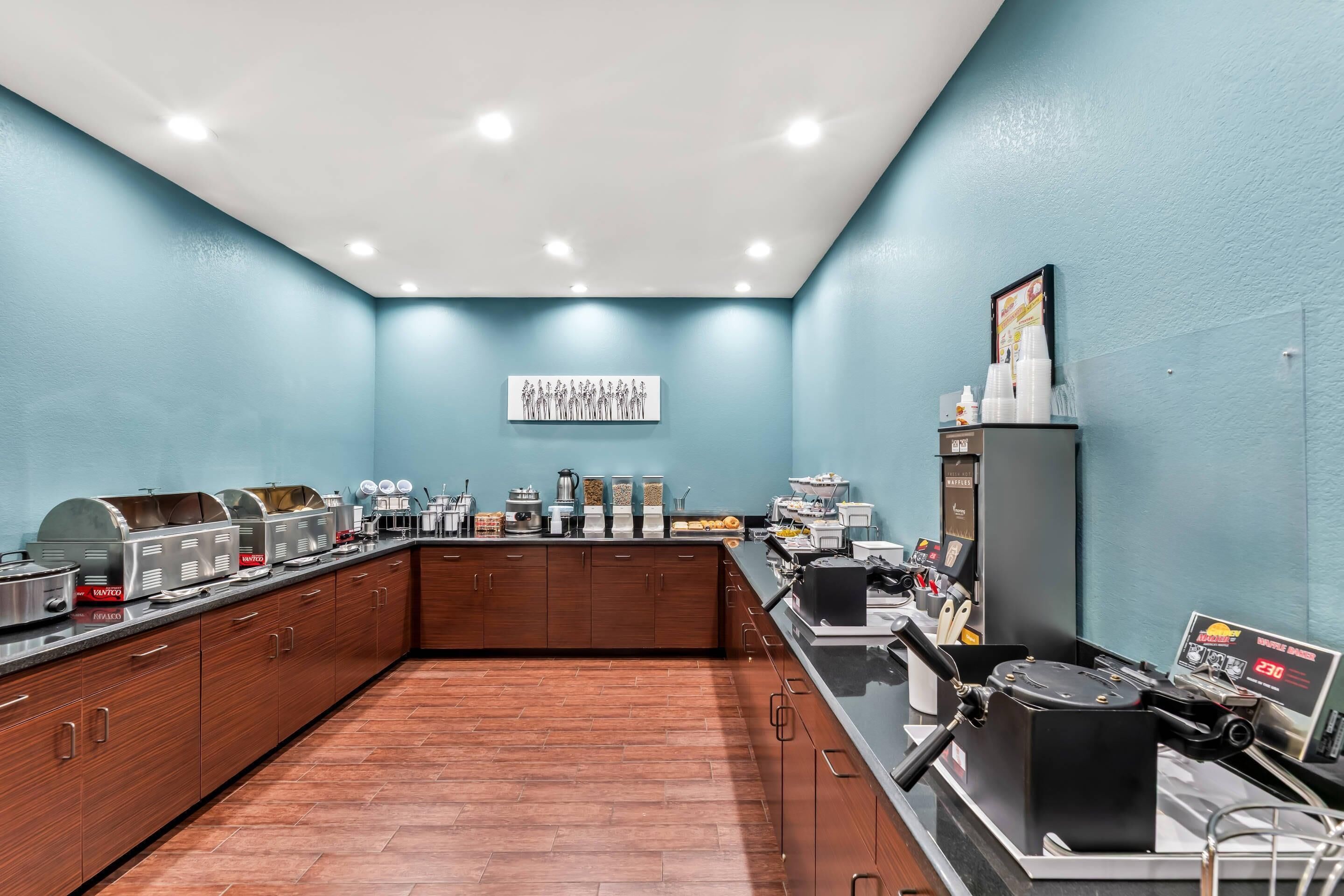 A kitchen with a long counter, various appliances, and a blue wall with a group photo.