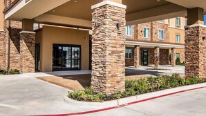 A hotel entrance with stone pillars, a covered walkway, and a landscaped area with plants.