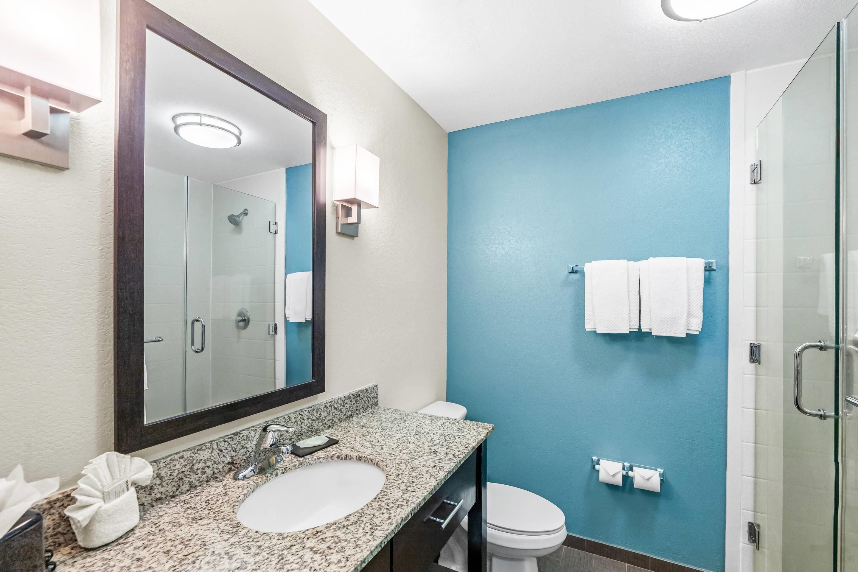 A modern bathroom with a granite sink, white toilet, and a glass shower enclosure.