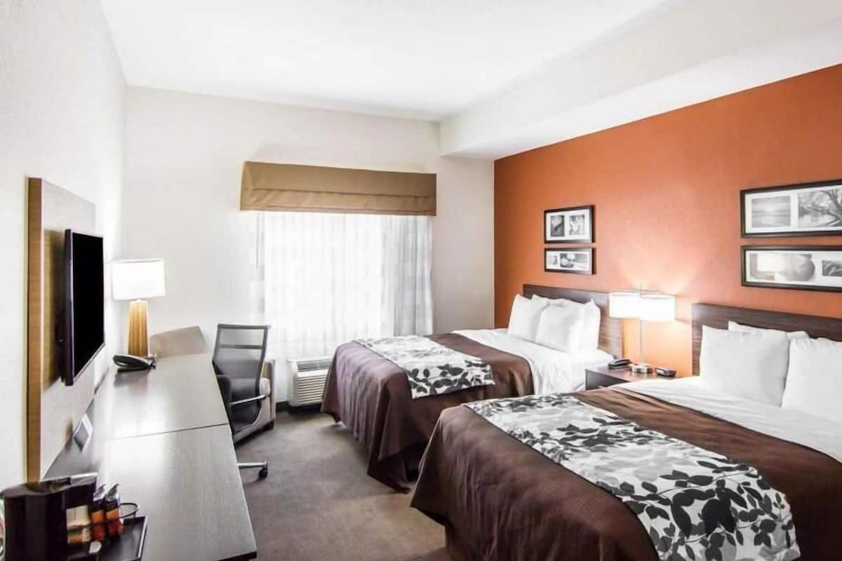 A hotel room with two beds, a desk, a chair, a TV, and a window with curtains.