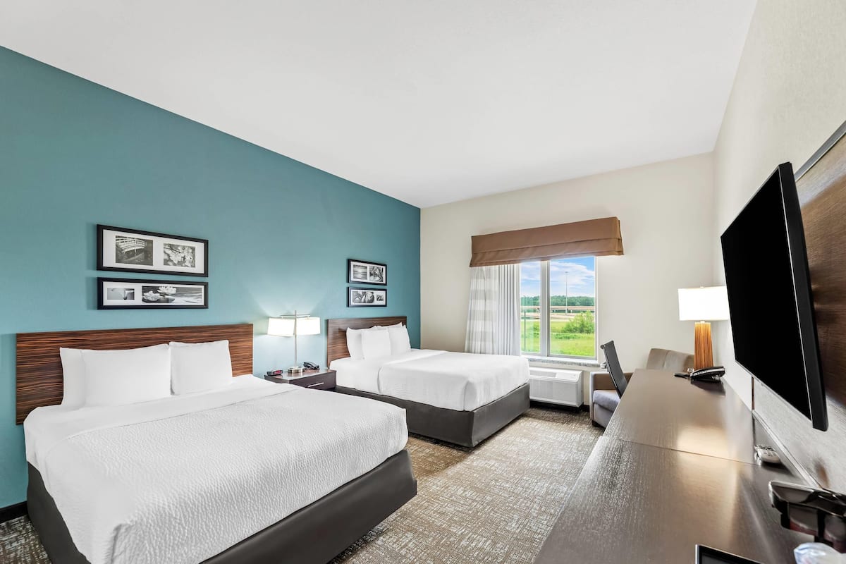 A hotel room with two beds, a desk, a TV, and a window with a view of the outdoors.