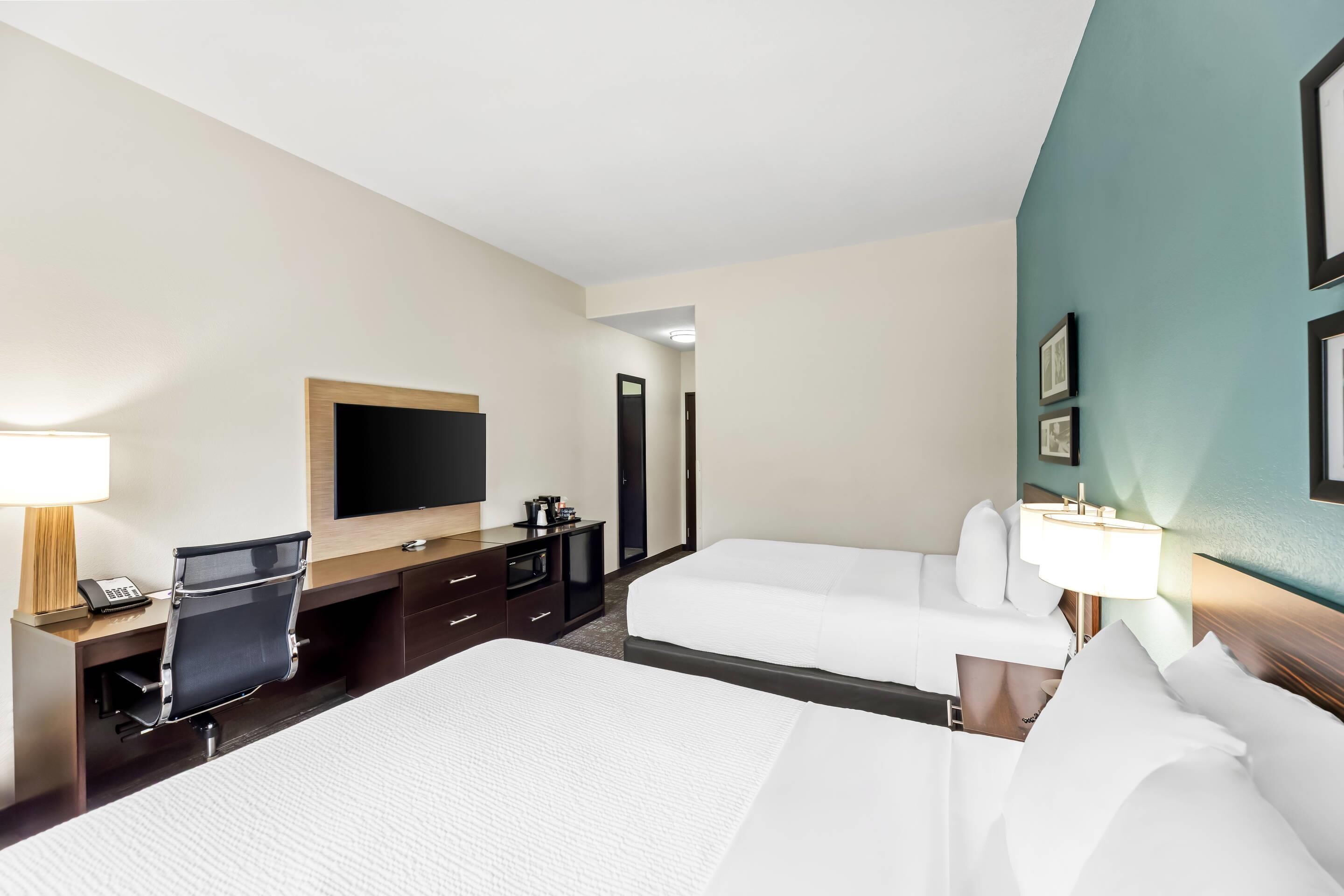 Een hotelkamer met een bed, een bureau met stoel, een televisie en een nachtkastje met lamp.