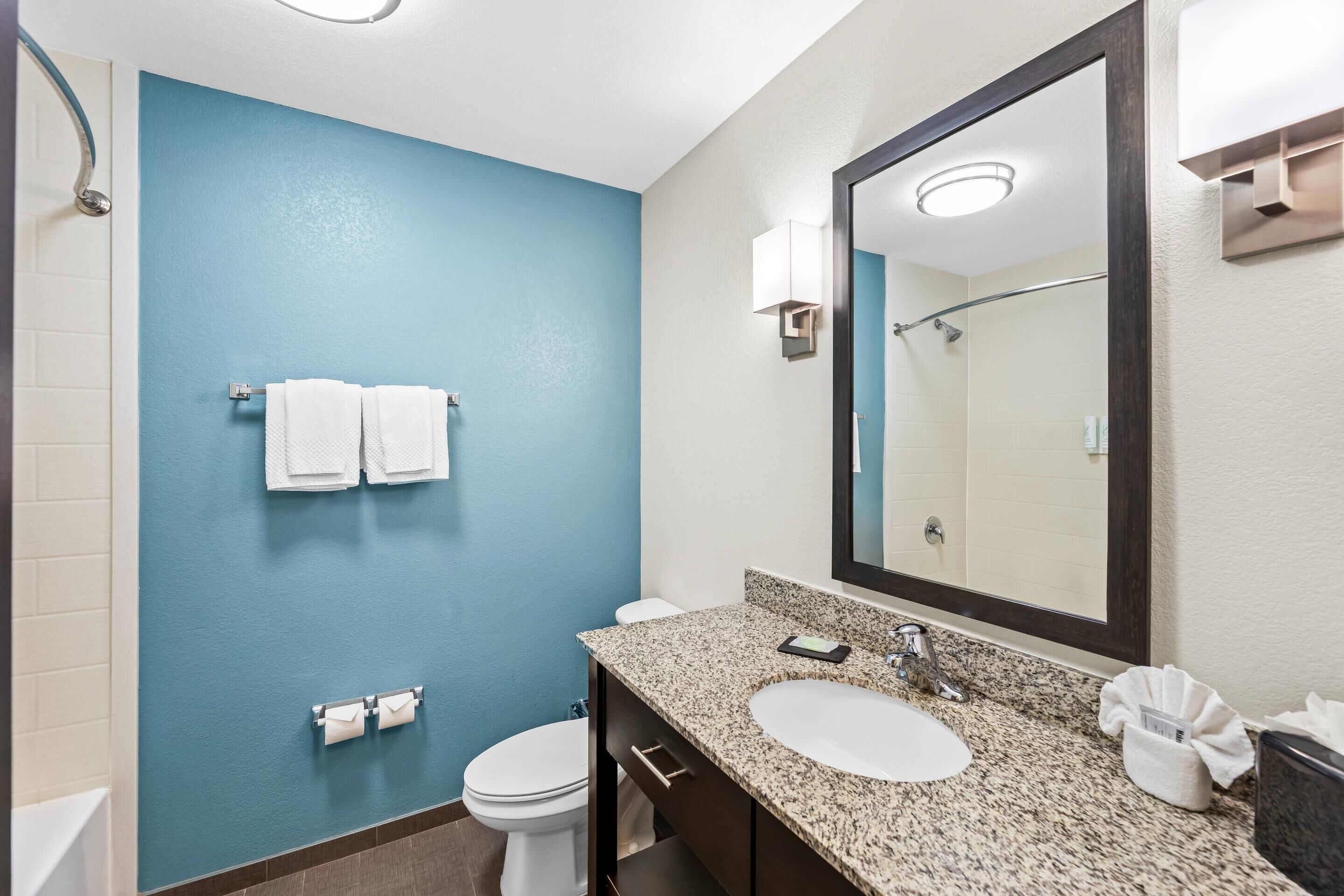 Un baño con pared azul, inodoro blanco y lavamanos con un espejo grande.