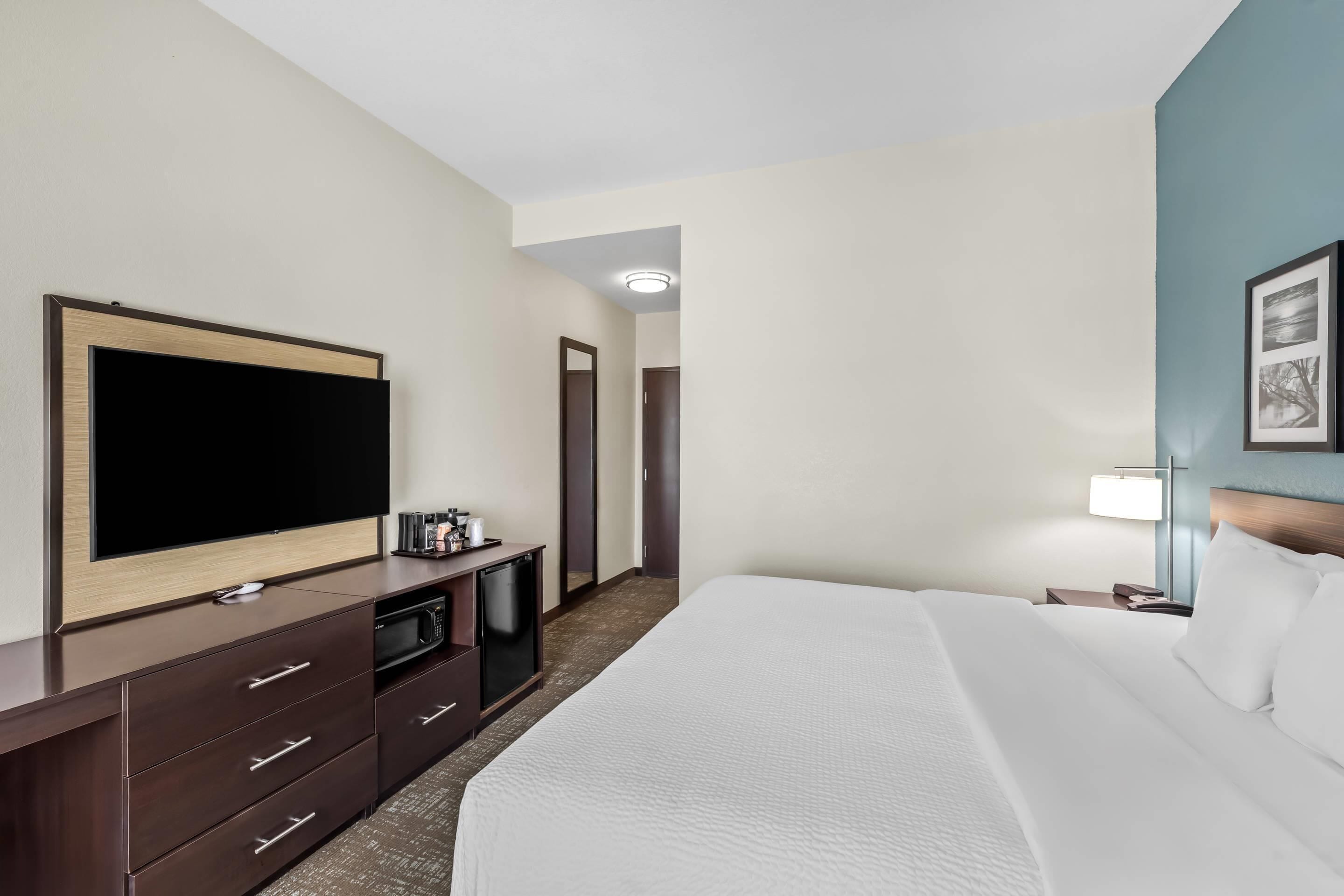 Et hotelværelse med en stor seng, et fladskærms-tv, en minibar og et skrivebord med lampe.