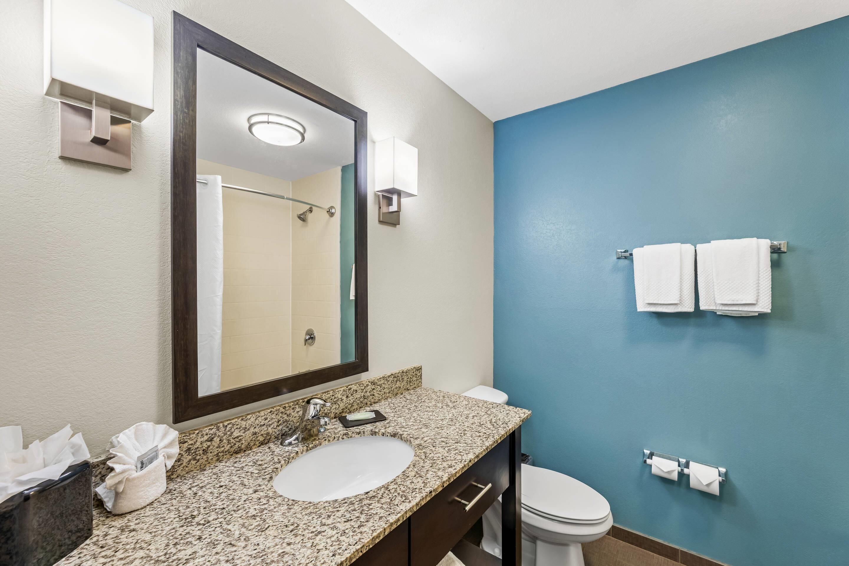 A bathroom with a granite countertop sink, a large mirror, a white toilet, and blue walls.