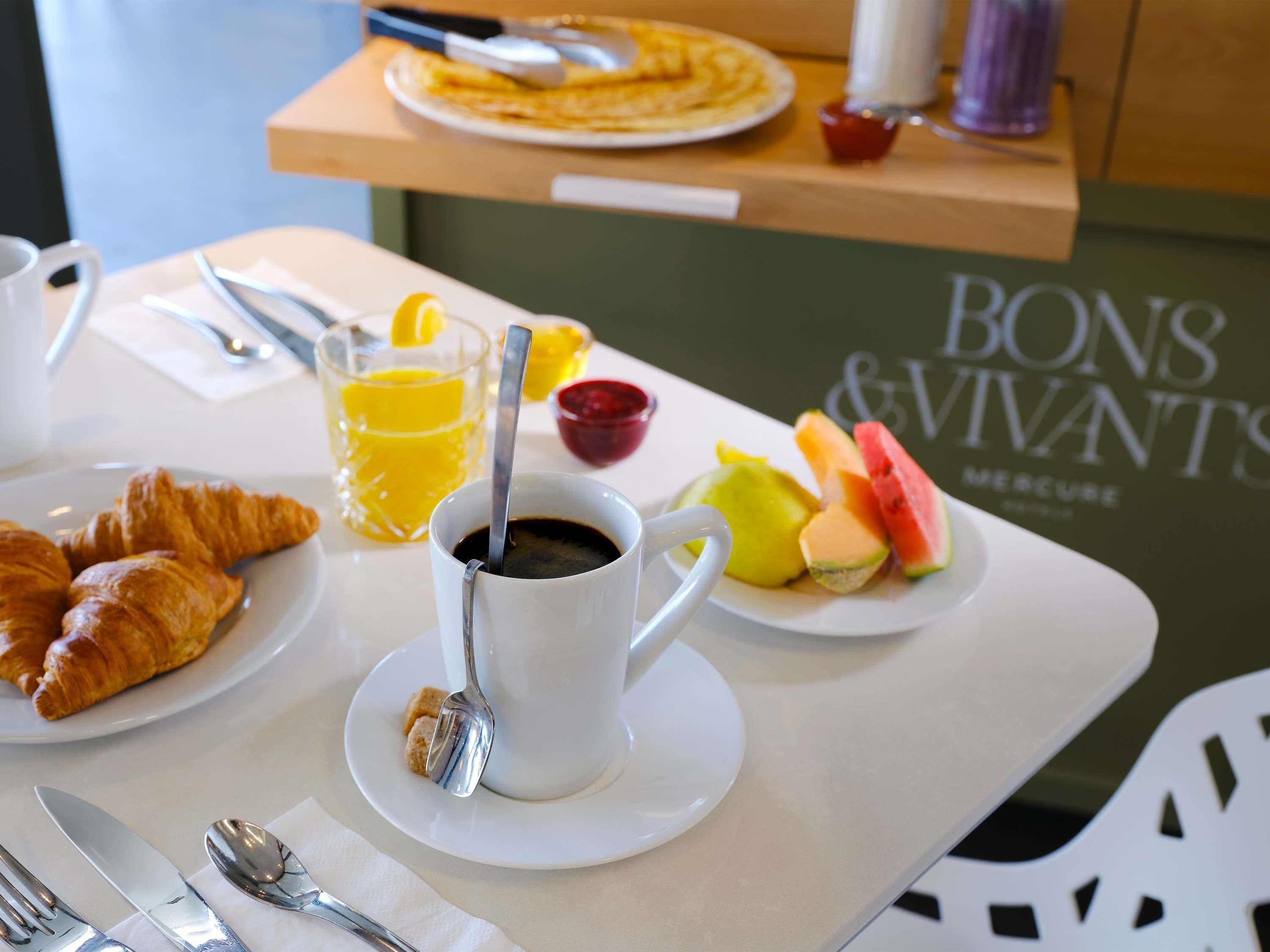 A breakfast setting with croissants, a cup of coffee, a glass of orange juice, and a plate of fruit.