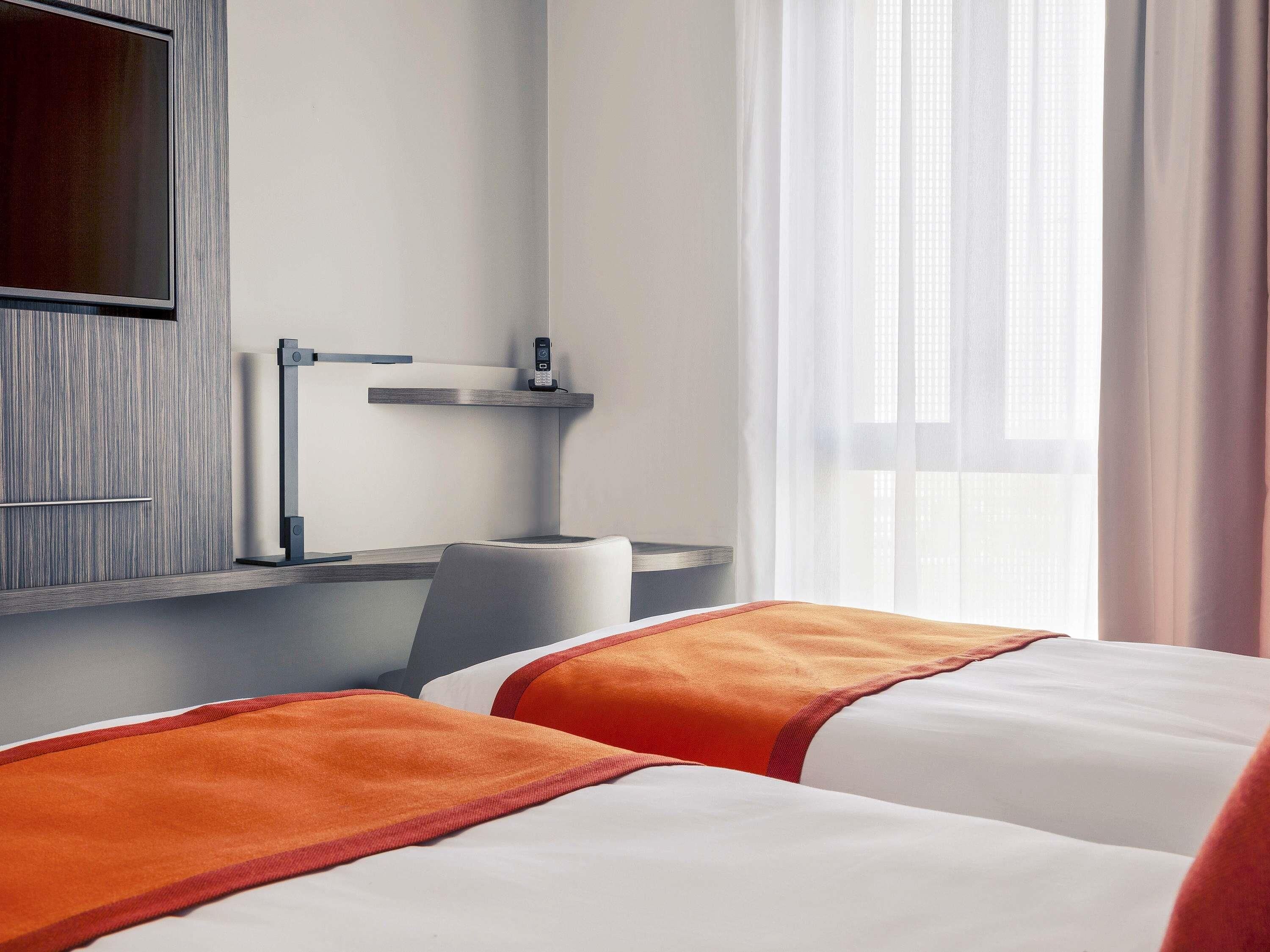 Quarto de hotel com cama, escrivaninha, cadeira e telefone.