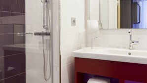 A modern bathroom with a glass-enclosed shower, a white sink, and a red vanity with shelves for towels.