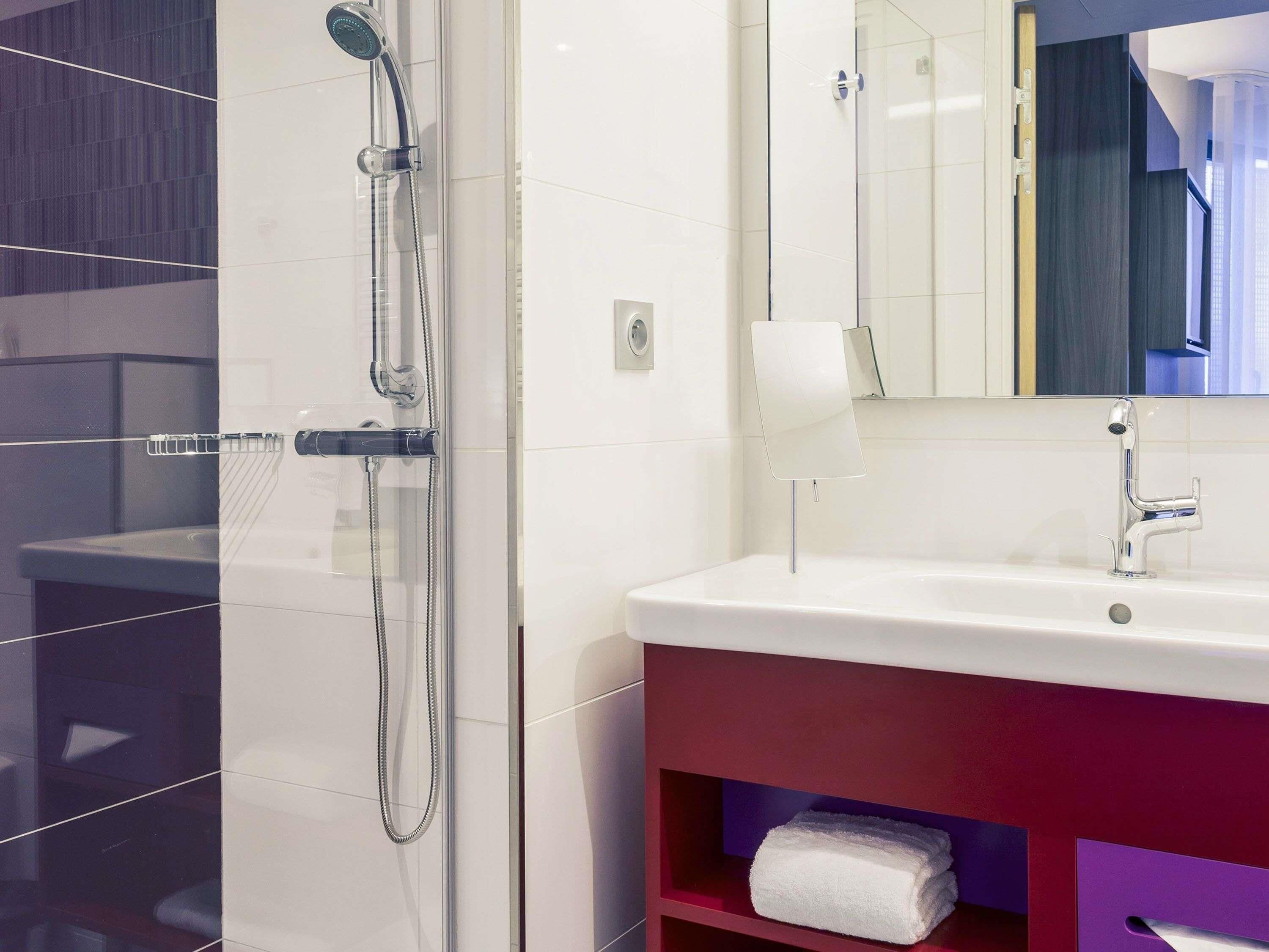 A modern bathroom with a glass-enclosed shower, a white sink, and a red vanity.