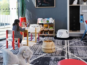 Un niño jugando con juguetes en una habitación con una estantería, una pizarra y un suelo estampado.