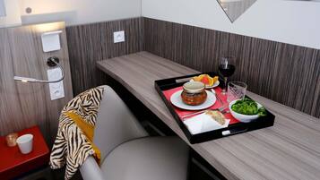 Una habitación pequeña con una pared decorada en madera, una mesita con una bandeja de comida, una silla y una toalla colgada en el respaldo.
