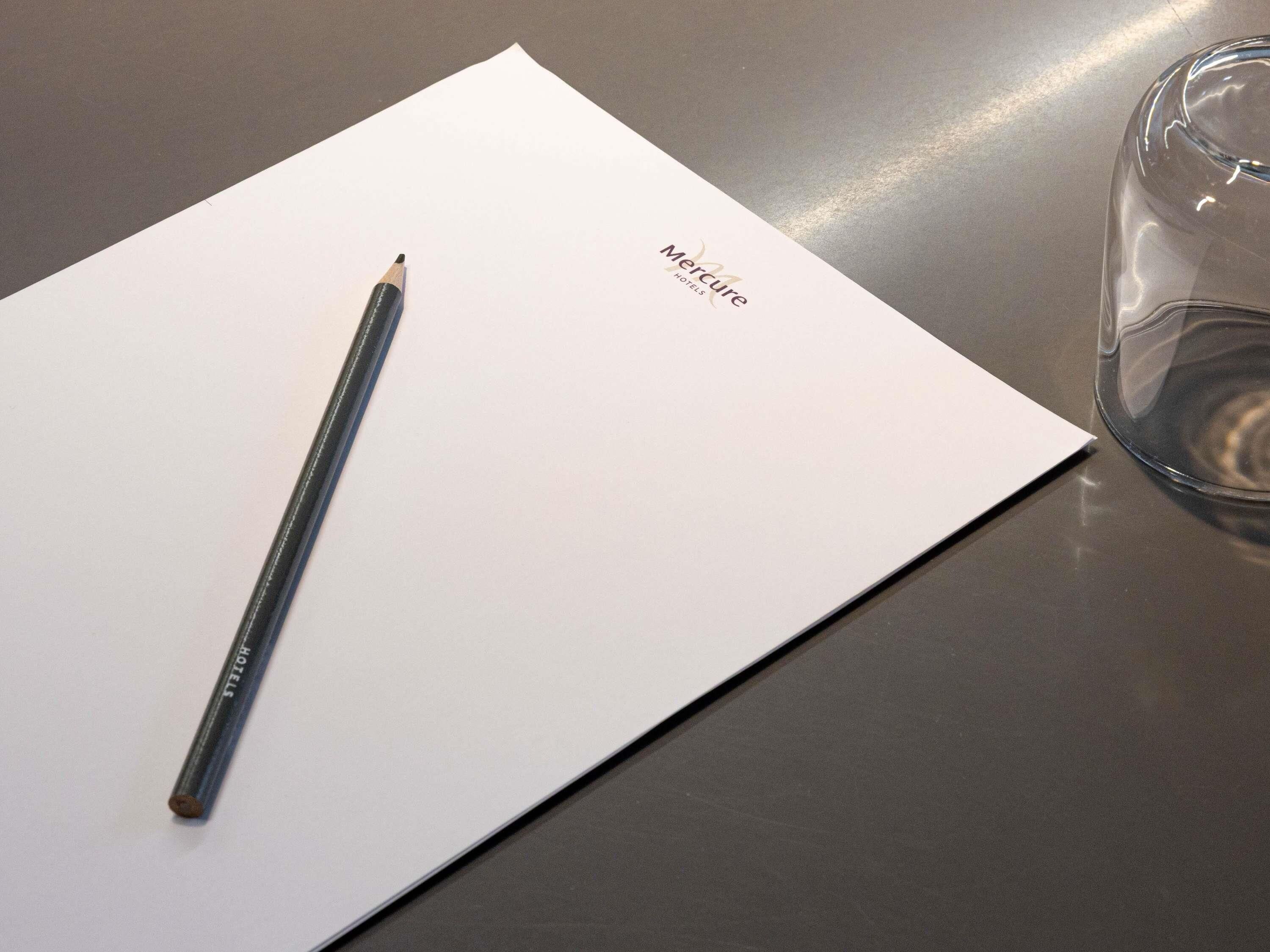 Eine Mercure Hotelbroschüre auf einem Tisch mit einem Bleistift und einem Glas.