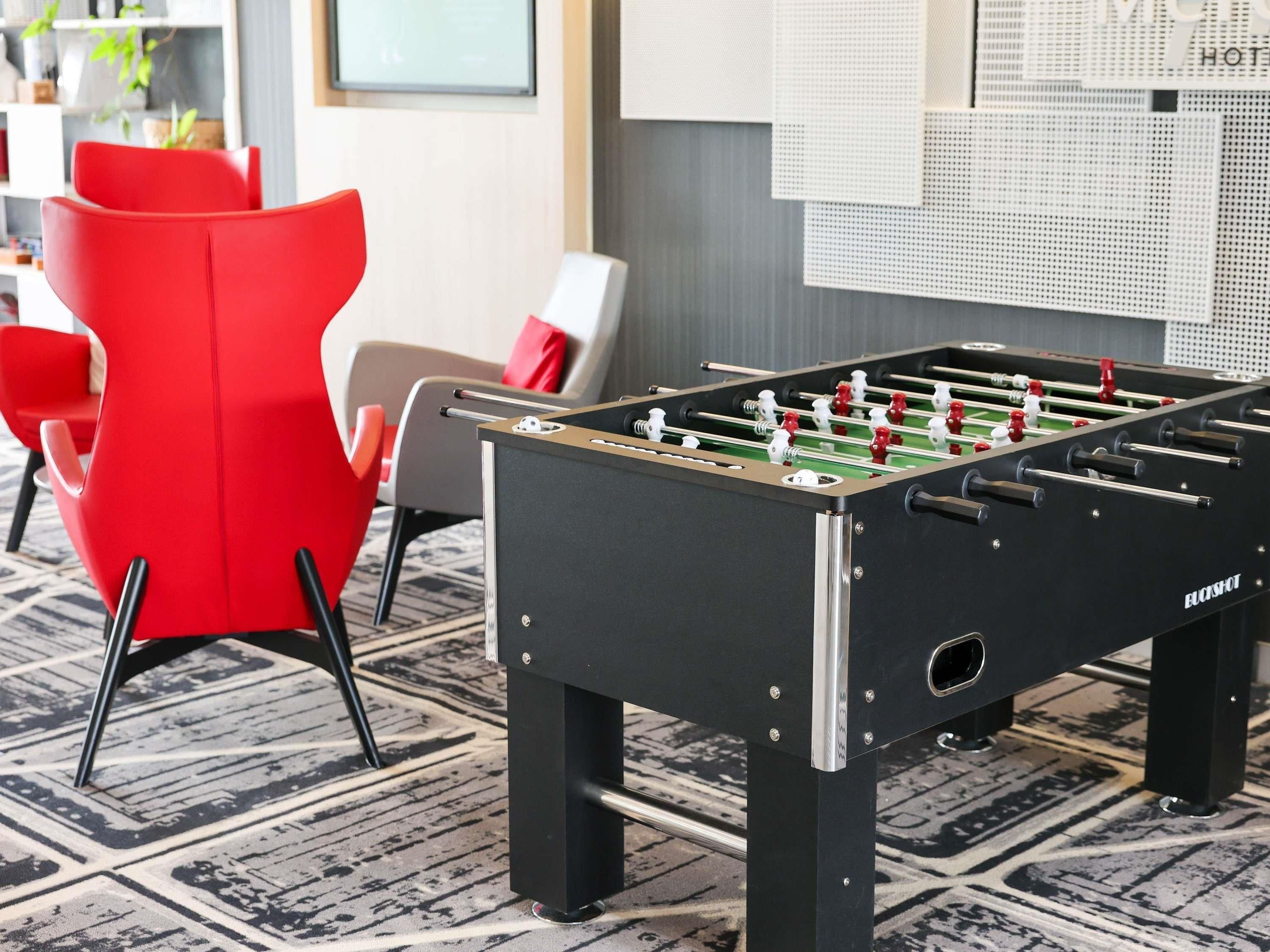 A foosball table in a room with modern furniture and a bulletin board in the background.