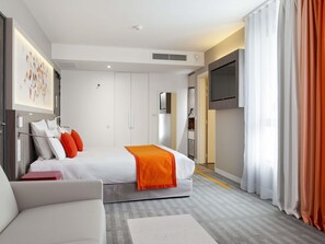 A modern hotel room with a bed, a TV, a sofa, and a large window with curtains. - Hôtel Mercure Toulouse Sud (Toulouse)