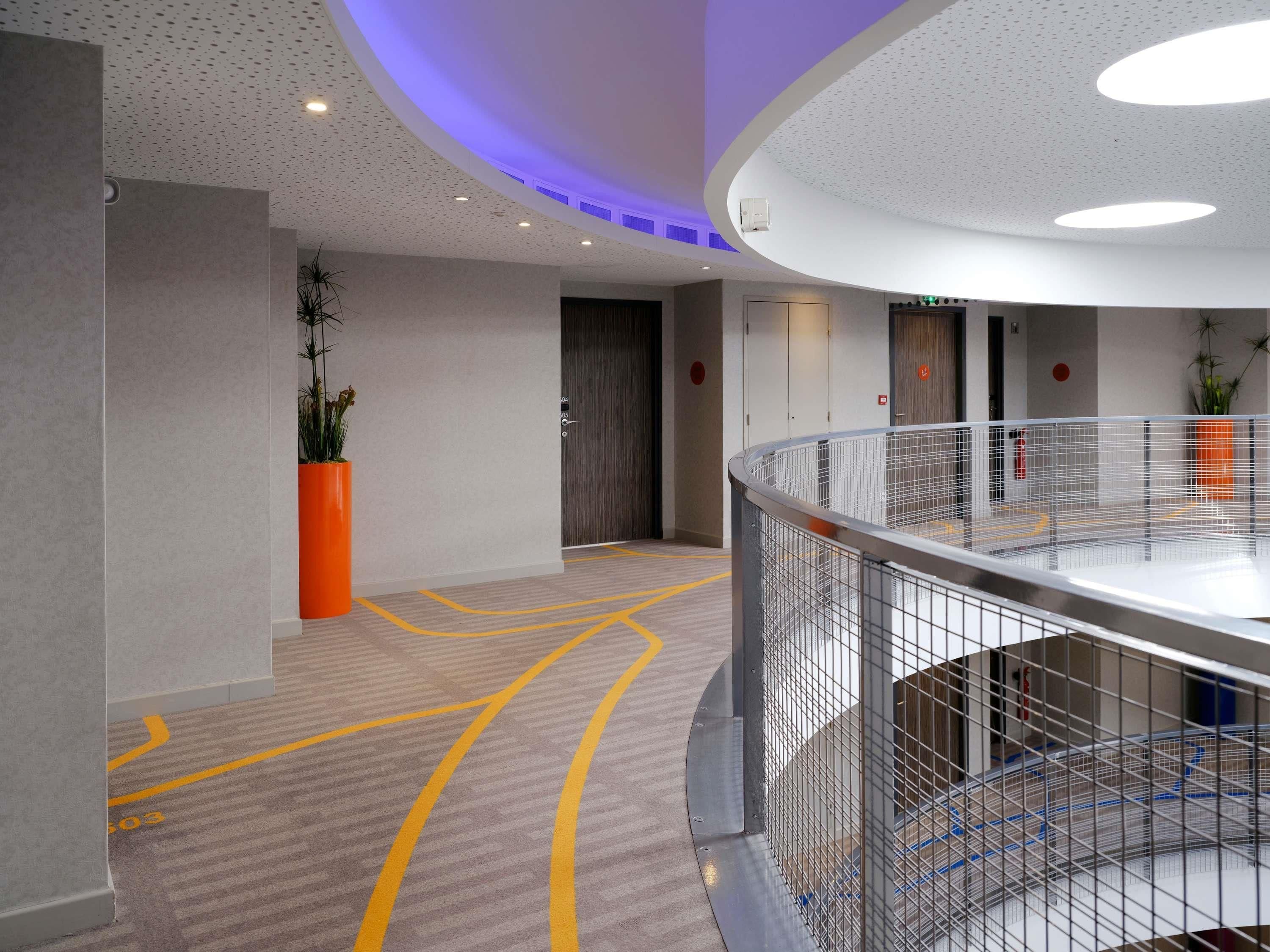 A modern hotel lobby with a curved railing, a potted plant, and a clear pathway marked with yellow lines.