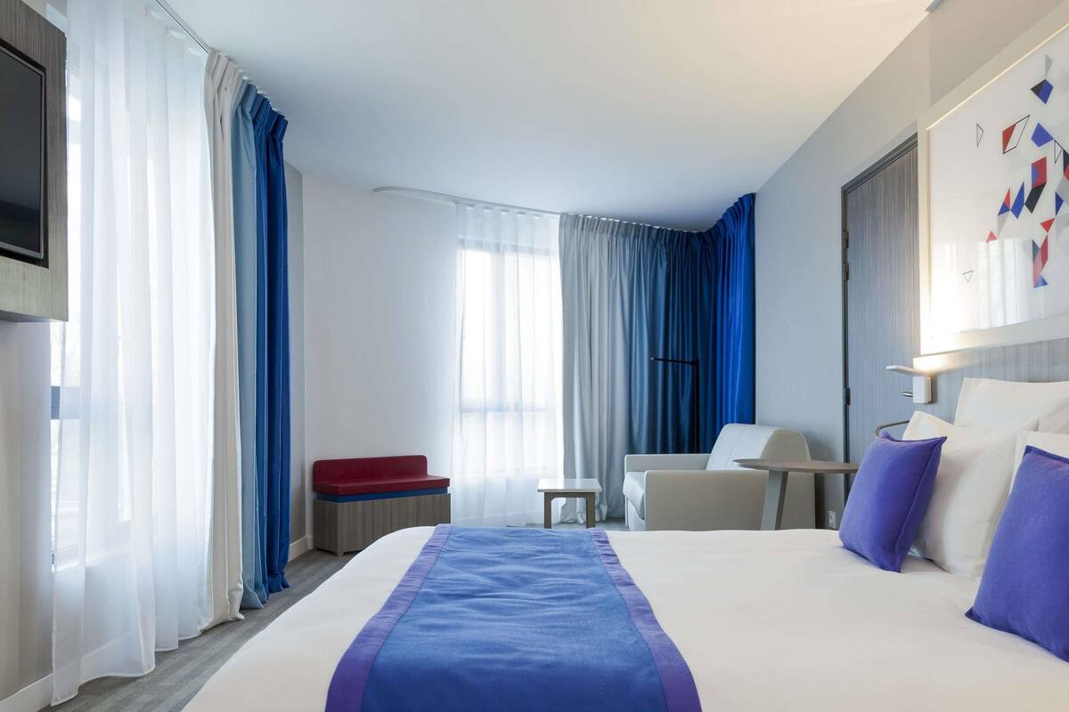 A hotel room with a large bed, a desk, a chair, and a TV.