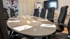 A conference room with a round table, black leather chairs, a flat-screen TV, and a red geometric wall decoration. - Hôtel Mercure Toulouse Sud (Toulouse)