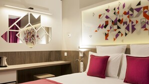 A hotel room with a bed, a desk, a mirror, and a wall with geometric patterns. - Hôtel Mercure Toulouse Sud (Toulouse)