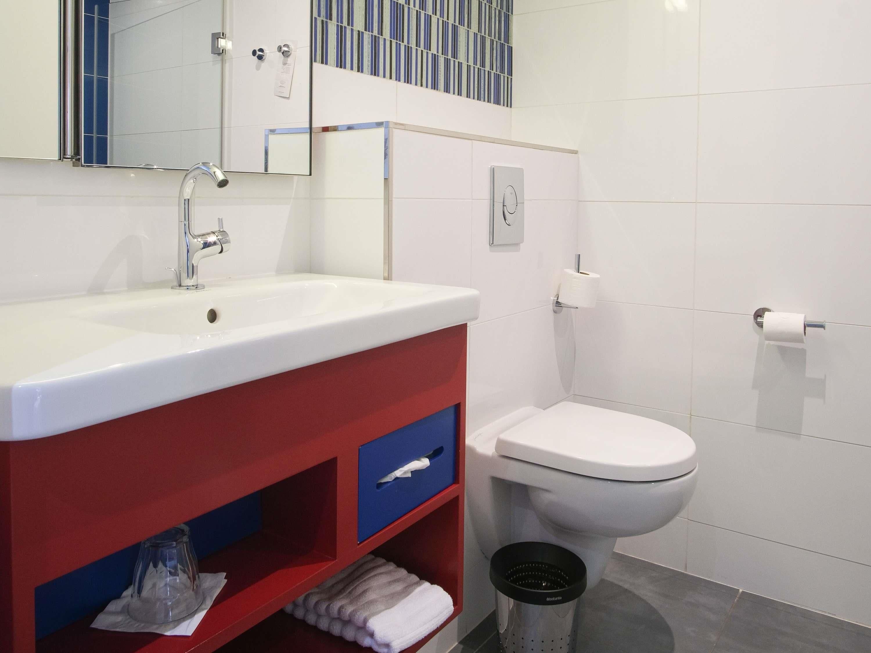 A bathroom with a white sink, red and blue vanity, a toilet, and a mirror.