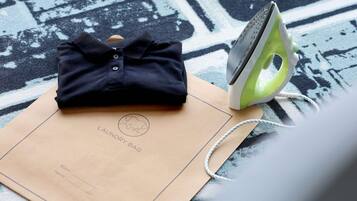 A neatly folded dark blue shirt on a brown paper bag with 'LAUNDRY BAG' printed on it, and a green and white iron on a patterned carpet.