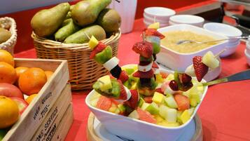 Una mesa de buffet con una variedad de frutas y un tazón de ensalada de frutas.