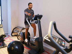 Una persona usando una máquina elíptica en una habitación que tiene una cinta de correr, una bicicleta estática y una pelota de ejercicios grande.