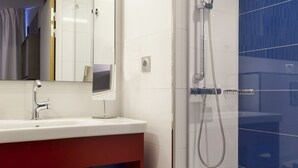 A modern bathroom with a glass-enclosed shower, a white sink with a red vanity, and a large mirror above the vanity.