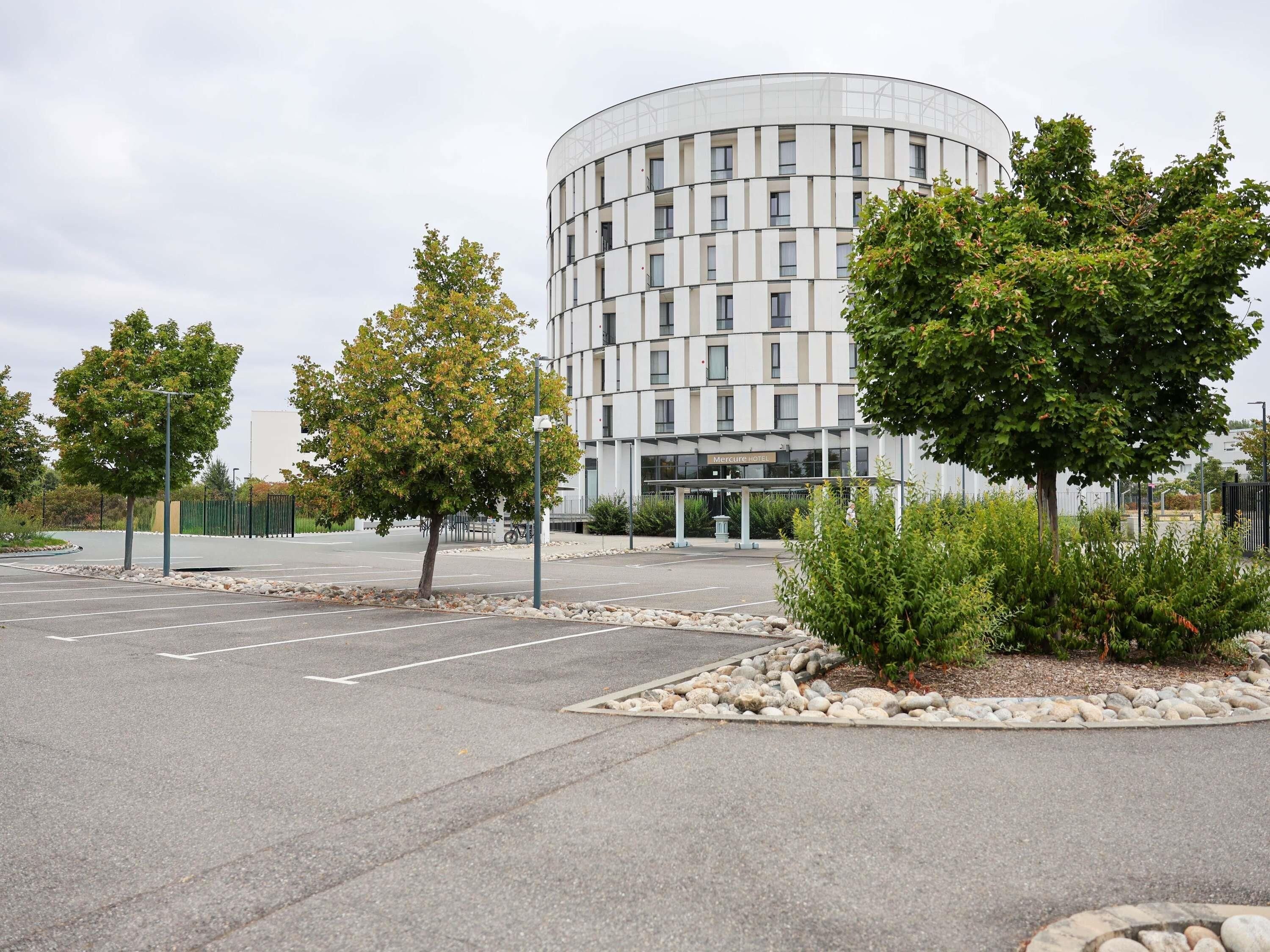A modern hotel with a circular building, a parking lot, and landscaped areas with trees.