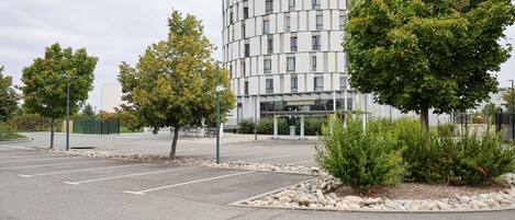A modern hotel with a circular building, a parking lot, and landscaped areas with trees.