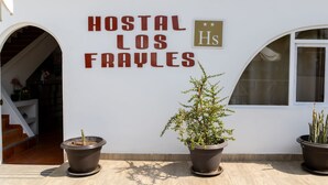 A building with a sign reading "HOSTAL LOS FRAYLES" and three potted plants in front. - Hostal Los Frayles (Paracas)