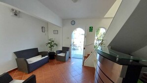 A reception area with a sofa, chairs, a desk, and a staircase leading to an outdoor area. - Hostal Los Frayles (Paracas)