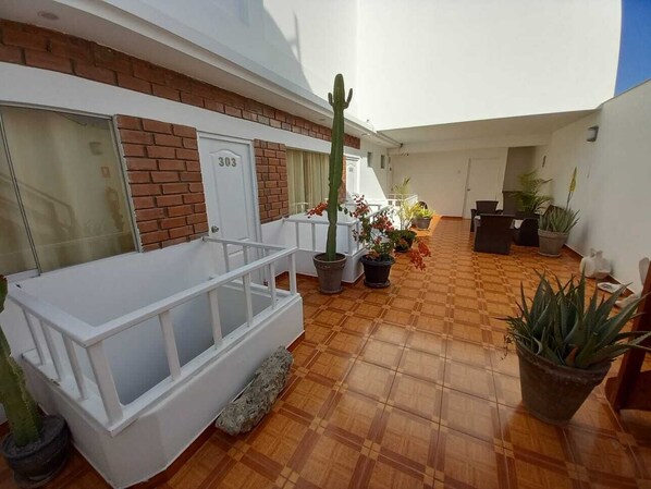 Un patio con un banco blanco, plantas en macetas y un cactus.