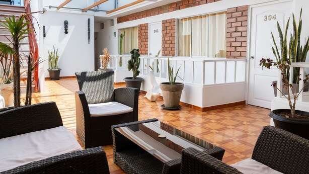 A spacious indoor area with wicker furniture, potted plants, and a reception desk. - Hostal Los Frayles (Paracas)