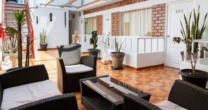 Amplio espacio interior con mobiliario de mimbre, plantas en macetas y una mesa de recepción.
