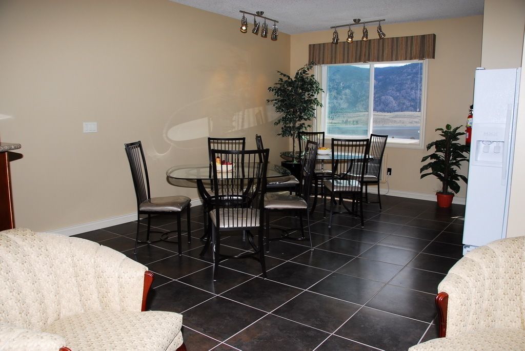 A dining area with a round table and six chairs, a refrigerator, and a window with a view of a mountainous landscape.