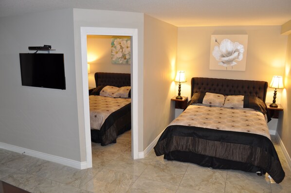 A hotel room with a large bed, two bedside tables with lamps, a flat-screen TV mounted on the wall, and a painting on the wall. - Ciliegia Villa (Osoyoos)