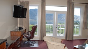 A hotel room with a desk, office chair, and a sofa. There is a television mounted on the wall and a view of a mountainous landscape through the windows. - Ciliegia Villa (Osoyoos)