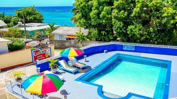 A hotel pool area with a view of the ocean, lounge chairs, and umbrellas. - Marine View Hotel (Ocho Rios)