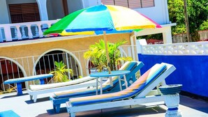 A pool area with lounge chairs and a table under a colorful umbrella. - Marine View Hotel (Ocho Rios)