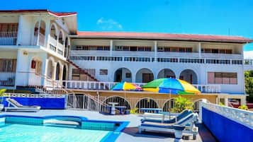 Un hotel con zona de piscina, varios balcones y tejado de tejas rojas.