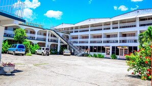 A multi-story building with a central staircase, a disco bar, and a parking area with several vehicles. - Marine View Hotel (Ocho Rios)