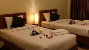 A hotel room with two beds, each with a wooden headboard, white bedding, and a small bedside table with a lamp. - Lita Place (Roi Et)