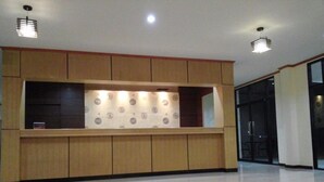 A reception area with a wooden counter, a patterned wall, and ceiling lights. - Lita Place (Roi Et)