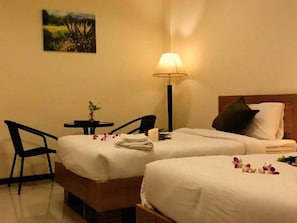 A hotel room with two beds, a nightstand, a lamp, a chair, and a small table with a plant.