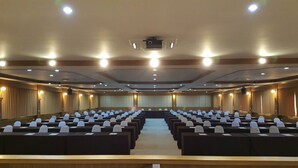 A conference room with rows of chairs, a stage at the front, and a ceiling-mounted projector. - Lita Place (Roi Et)