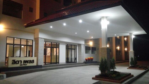 A hotel entrance with a covered outdoor area, large windows, and a signboard. - Lita Place (Roi Et)